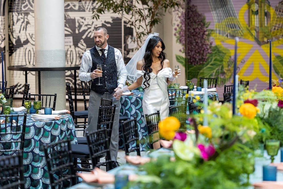 A bride and groom celebrating a wedding, holding hands and looking at decorations